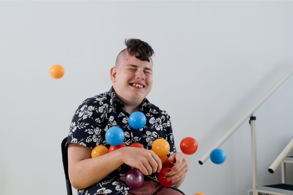 A happy teenager with cerebral palsy smiles while working on physical exercises with their supportive Careline 24 carer in a home setting.