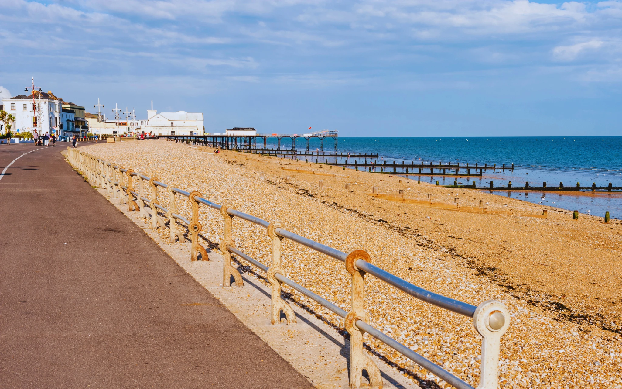 View of Bognor Regis seafront with the pier, promenade, and shingle beach under a bright blue sky.