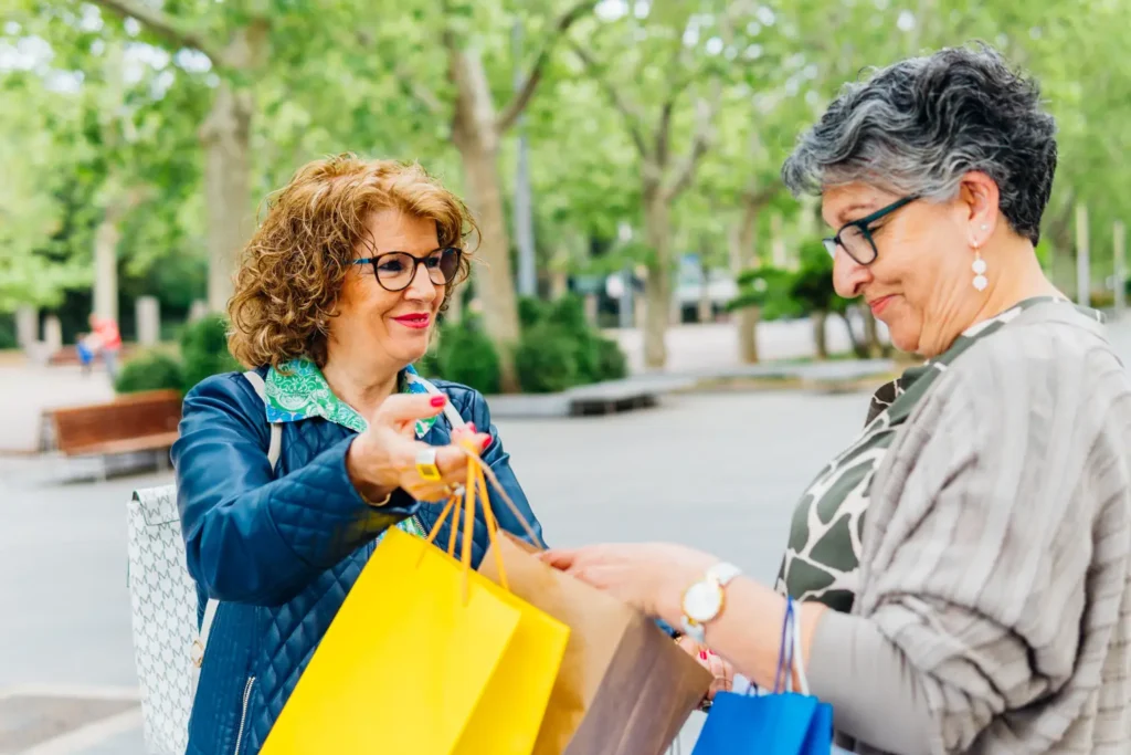  A professional female carer and her elderly client smile while carrying shopping bags together after a successful trip to local West Sussex shops.