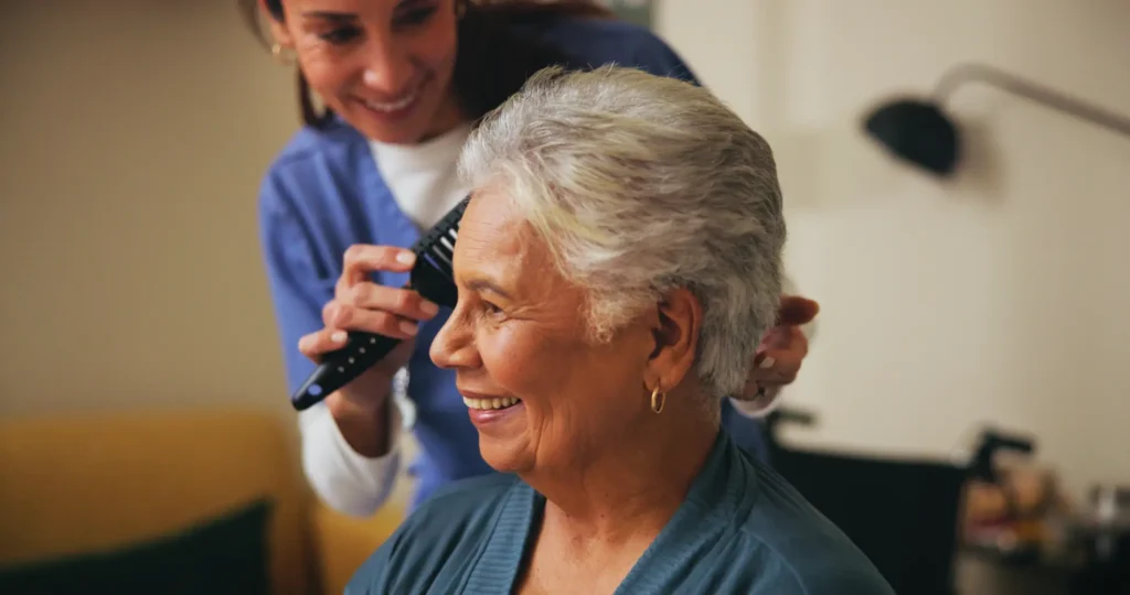 A compassionate carer from our small, consistent team gently assists an elderly lady with brushing her hair, providing supportive personal care in her own home.