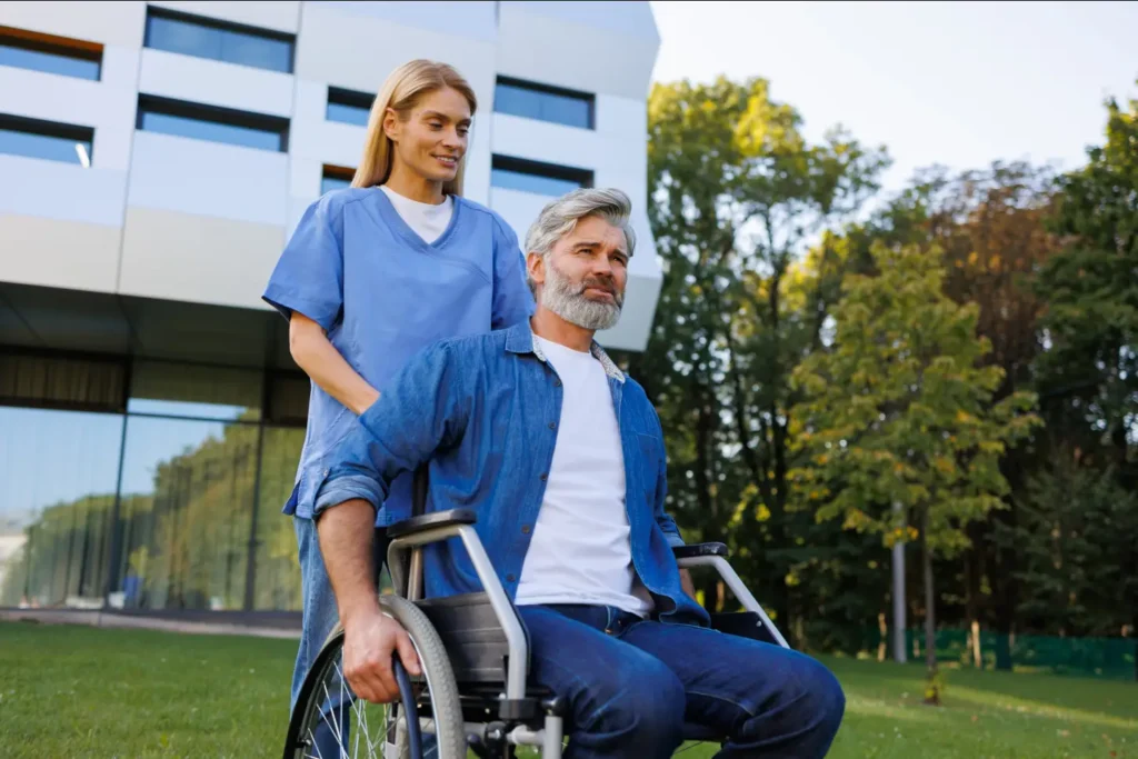 A cheerful Careline 24 carer and an elderly client enjoy a sunny, supportive walk together outdoors, promoting mobility and companionship in West Sussex.