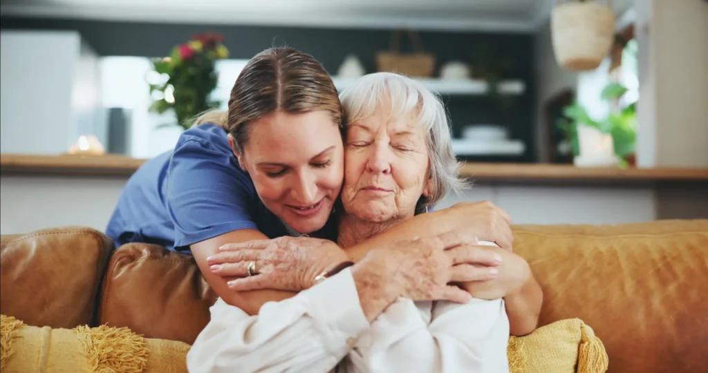 A compassionate Careline 24 carer sharing a warm, reassuring moment with an elderly client receiving dignified end-of-life care at home.