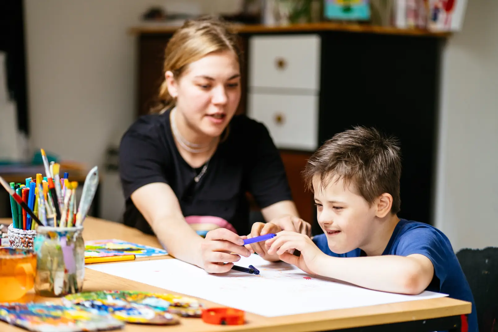 A compassionate Careline 24 carer providing one-to-one support to a young adult with a learning disability, patiently assisting with a homework task at a home desk.