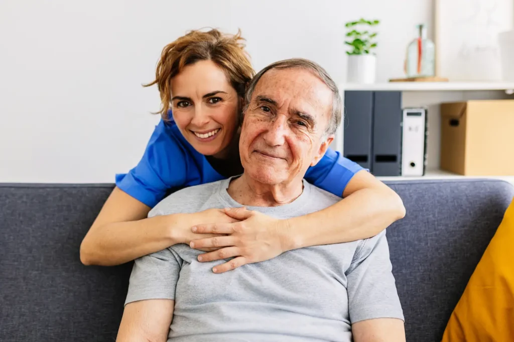 A compassionate female caregiver and her elderly client share a warm, joyful hug, illustrating the genuine friendship and trusted companionship provided by Careline 24.