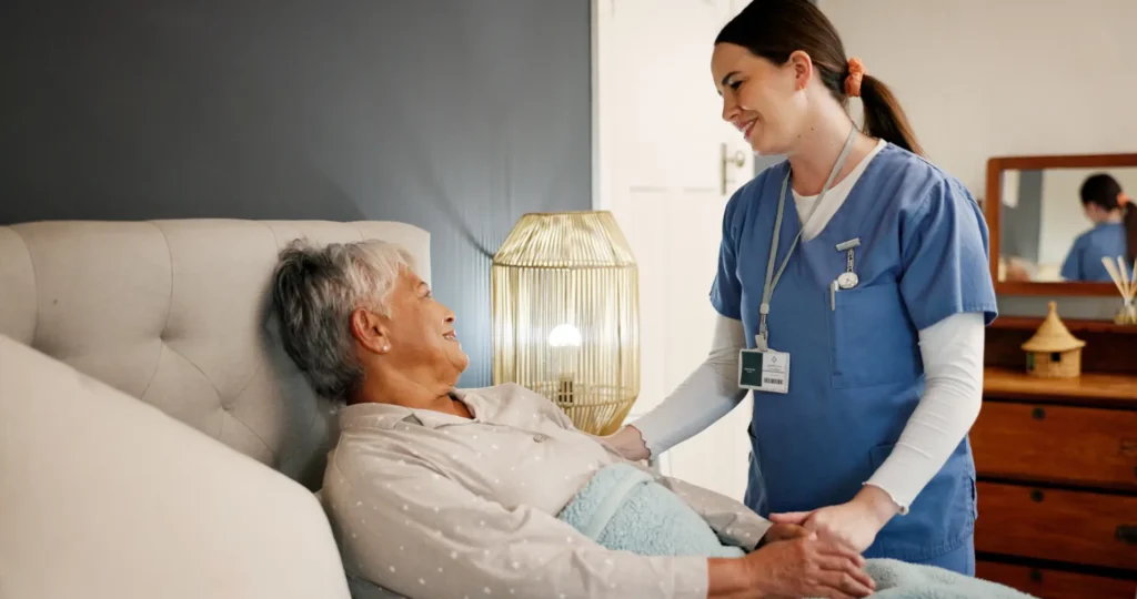 A compassionate Careline 24 carer providing gentle, dignified companionship and support to an elderly lady receiving end-of-life care in her own bedroom.