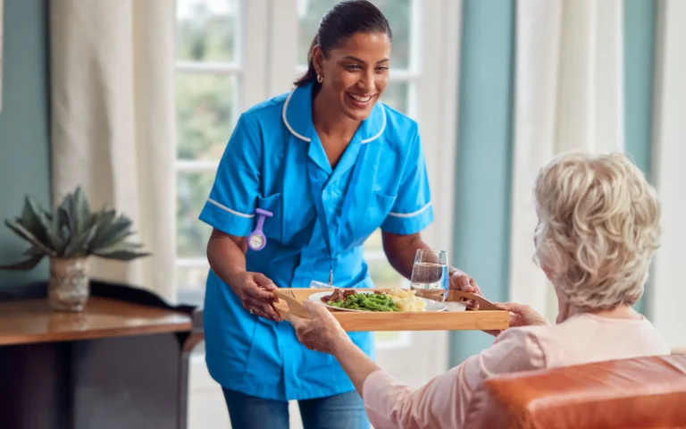 carer hands a tray with a hot meal and a glass of water to an older woman