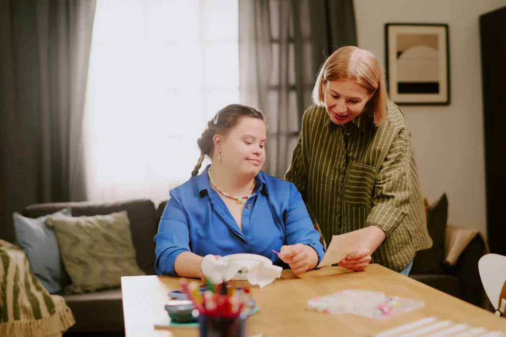 A mother and her adult daughter with a learning disability sharing a happy, focused moment while working on a creative embroidery project together at home.
