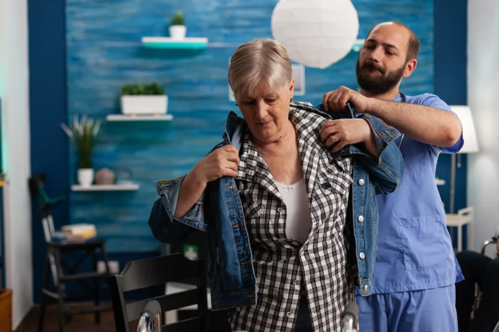 A professional male carer provides steady, supportive assistance to an elderly gentleman while walking indoors, ensuring his safety and promoting mobility.
