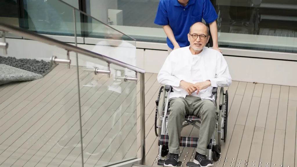  A compassionate Careline 24 carer in West Sussex supports a smiling elderly gentleman in a wheelchair, providing dignified post-discharge assistance to ensure a safe and supported return home.