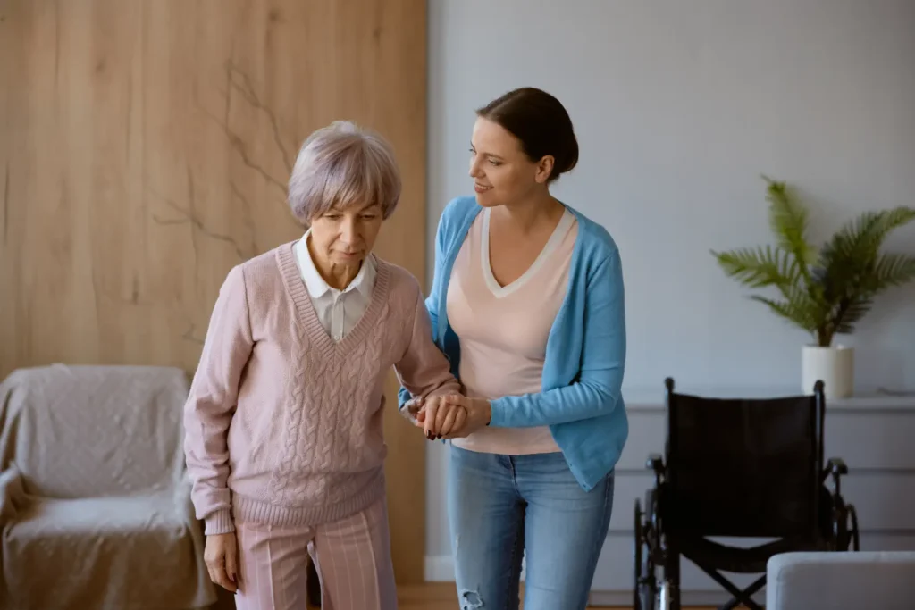 A professional Careline 24 carer provides steady, physical support to an elderly client while walking indoors, ensuring safety and promoting mobility in Chichester.