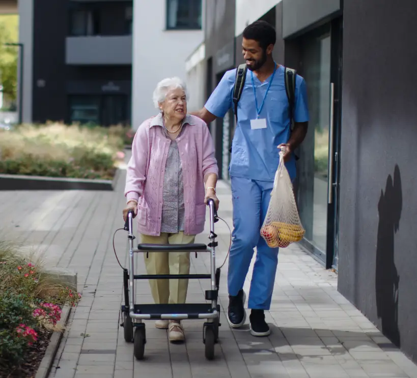 A cheerful, professional male carer returns with fresh groceries for a client, providing reliable shopping support as part of a consistent care team.
